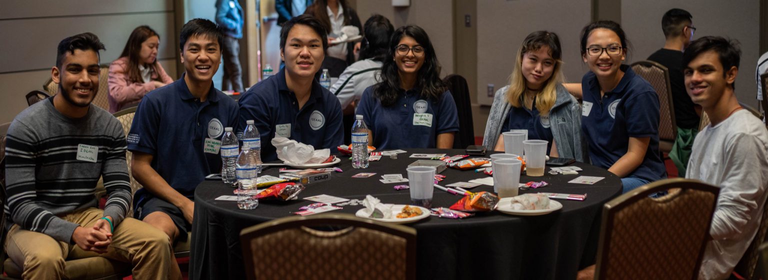Group of diverse students sitting together at a banquet, smiling at the camera. 