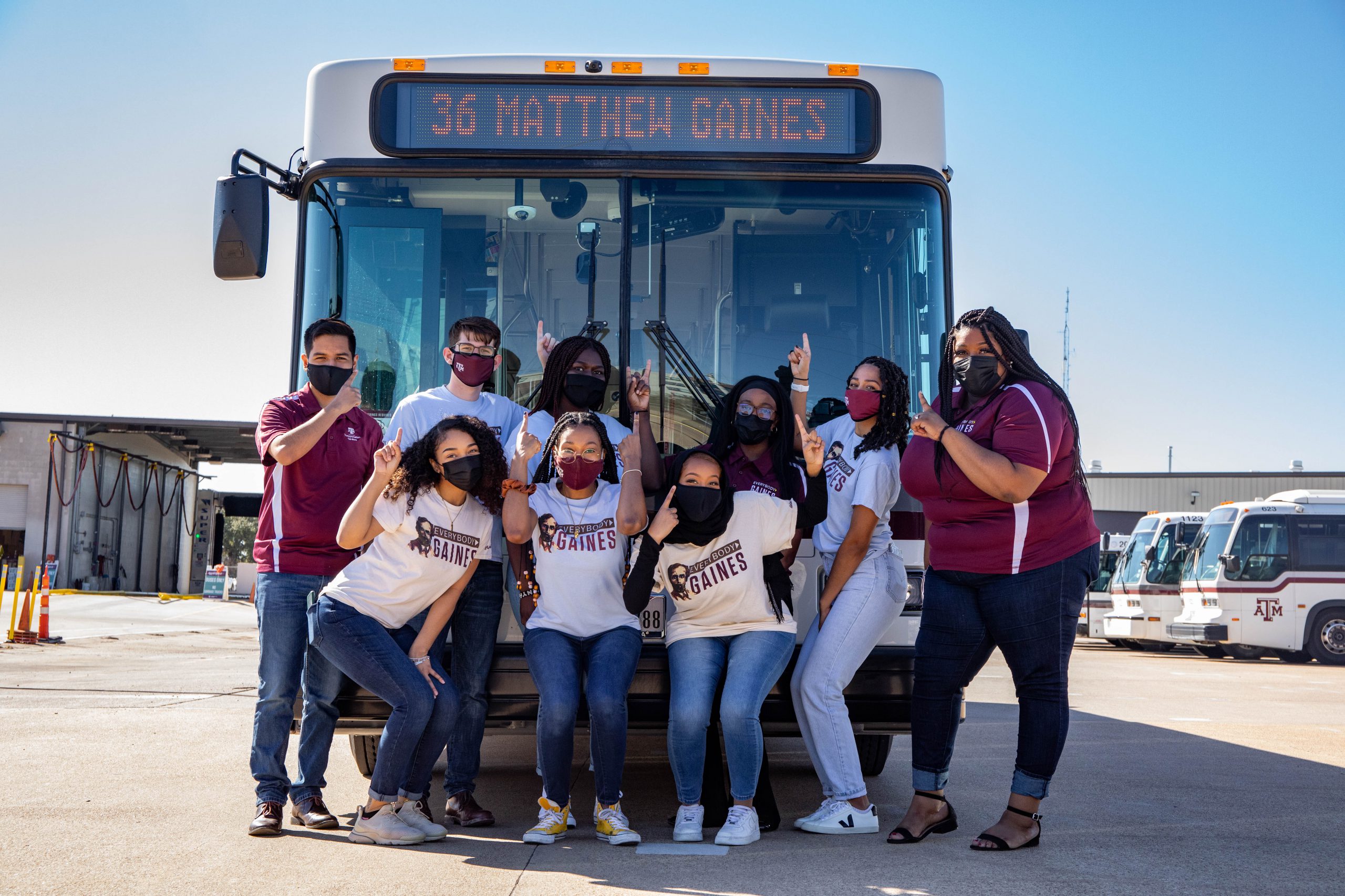 Image of the Matthew Gaines Society in front of an Aggie Spirit Bus displaying the newly named Matthew Gaines route on the bus marquee.
