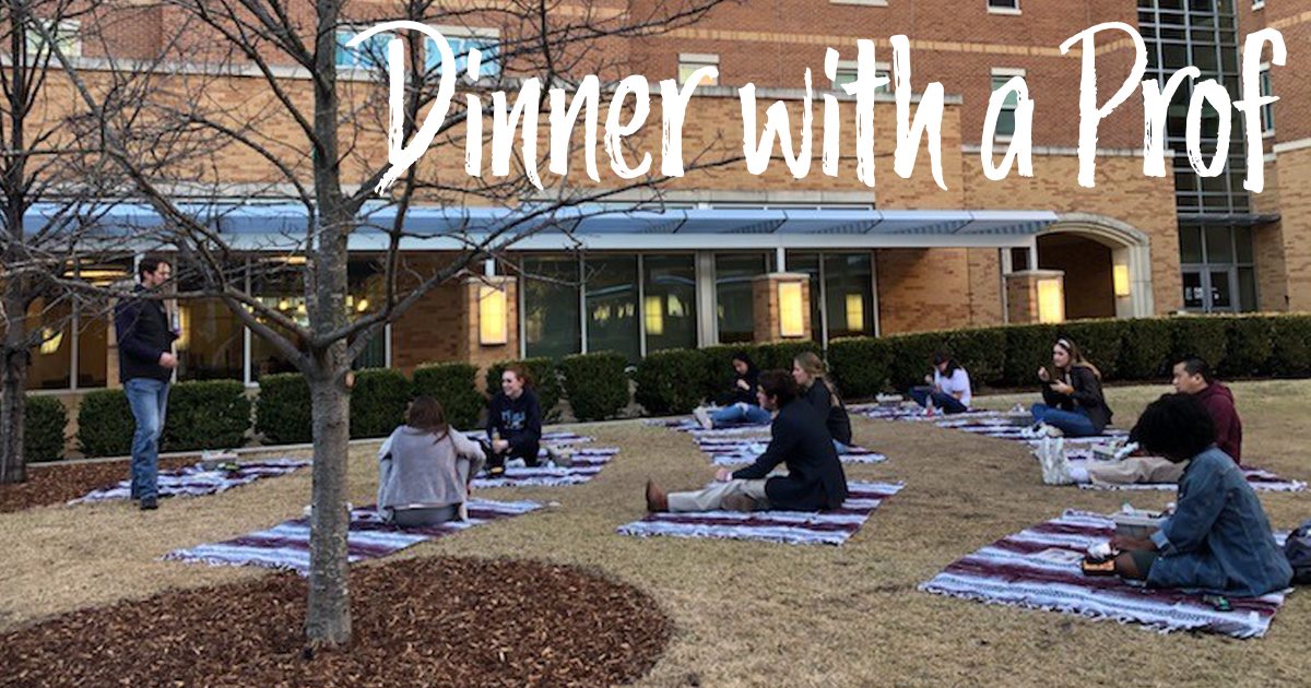 photo of students outside sitting on blankets eating dinner with a professor