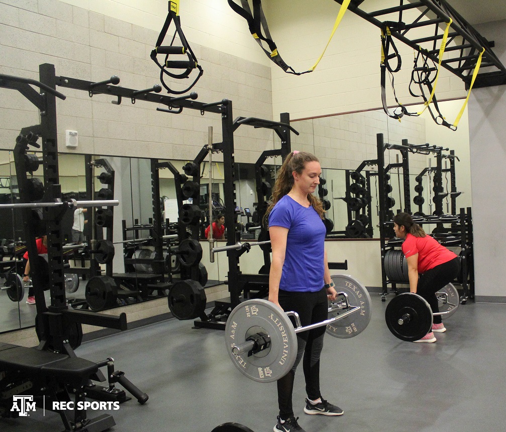 Student lifting a barbell with weights in the weight area of the rec center.