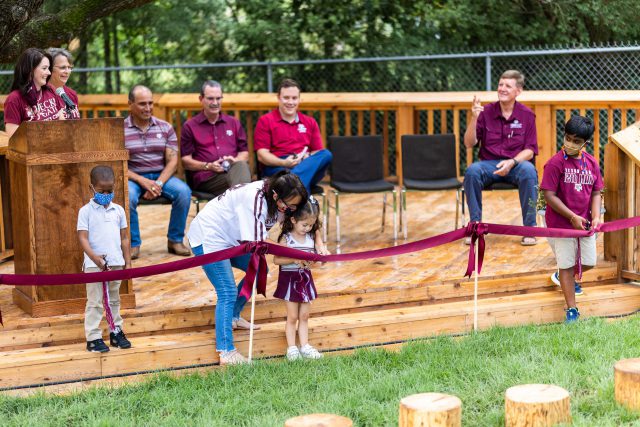 Students at the Becky Gates Children's Center use safety scissors to cut the ribbon during the ceremony celebrating the new nature playground