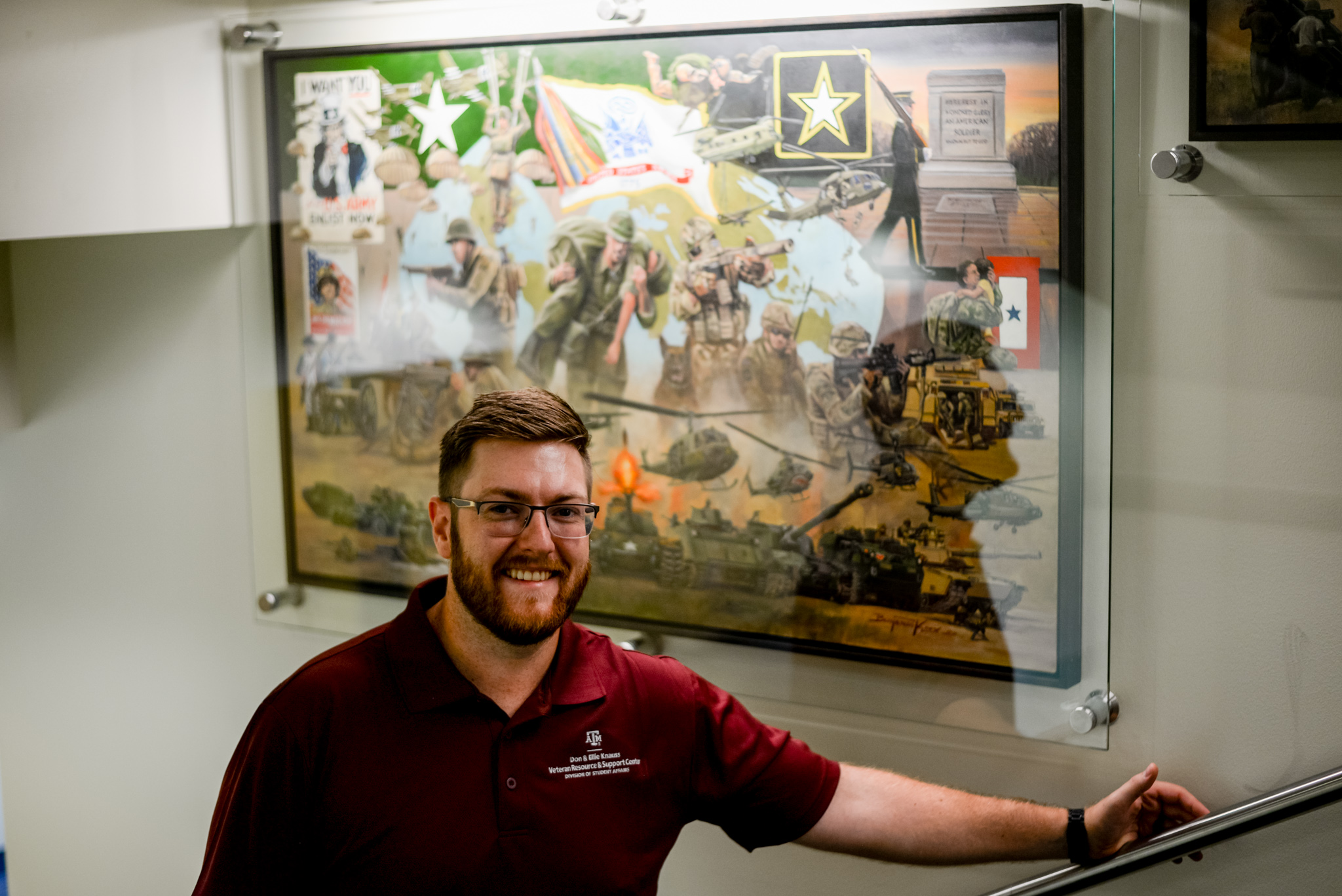 Dakota Kridler wears a maroon polo and smiles while standing in front of the U.S. Army portrait from the defenders of freedom series outside the VRSC.