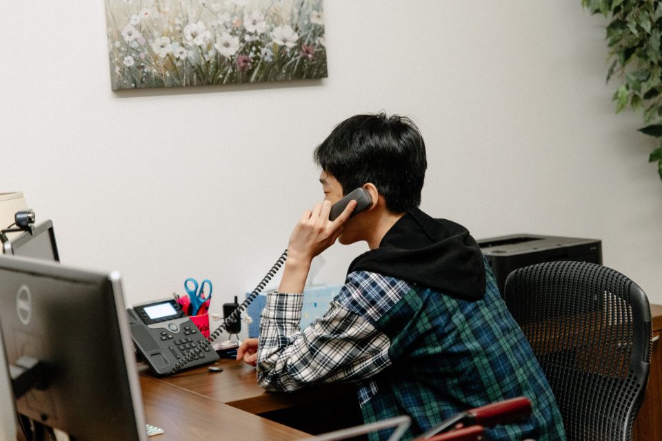 Julius Jang sits at his desk and answers phone calls during HelpLIne shift