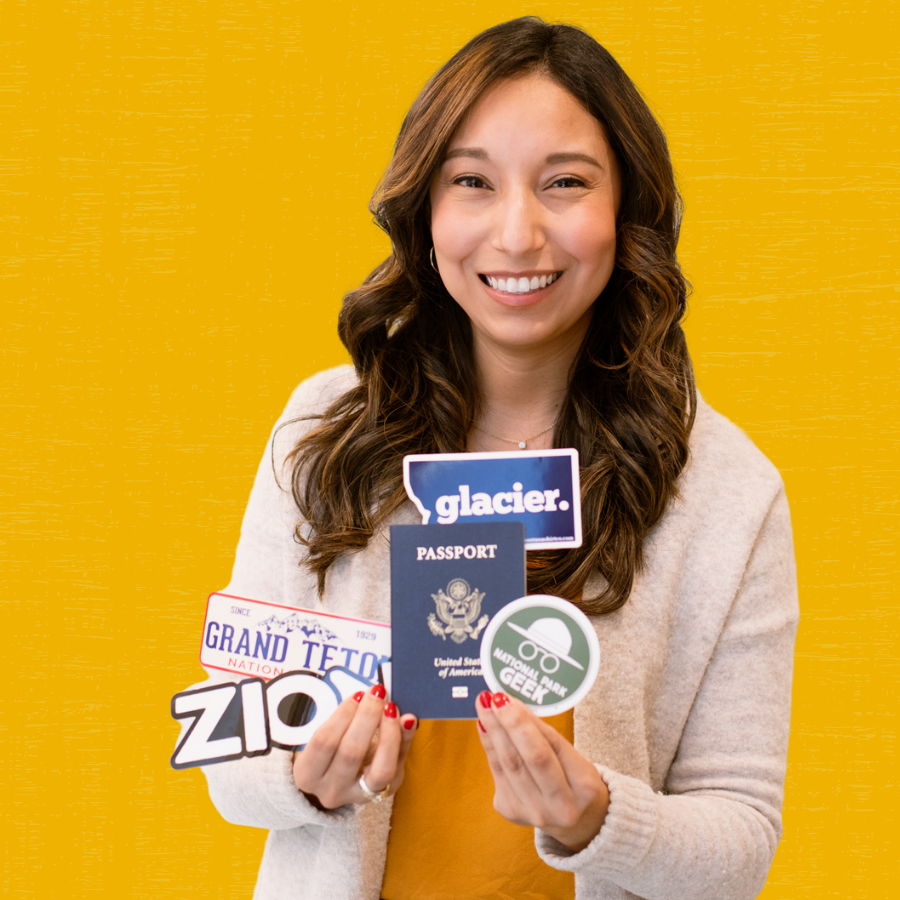 Ashley Ramirez holding up her passport with stickers from national parks she has visited.