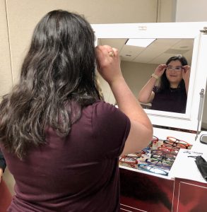 Photo of a student looking in the mirror as she tries on glasses.