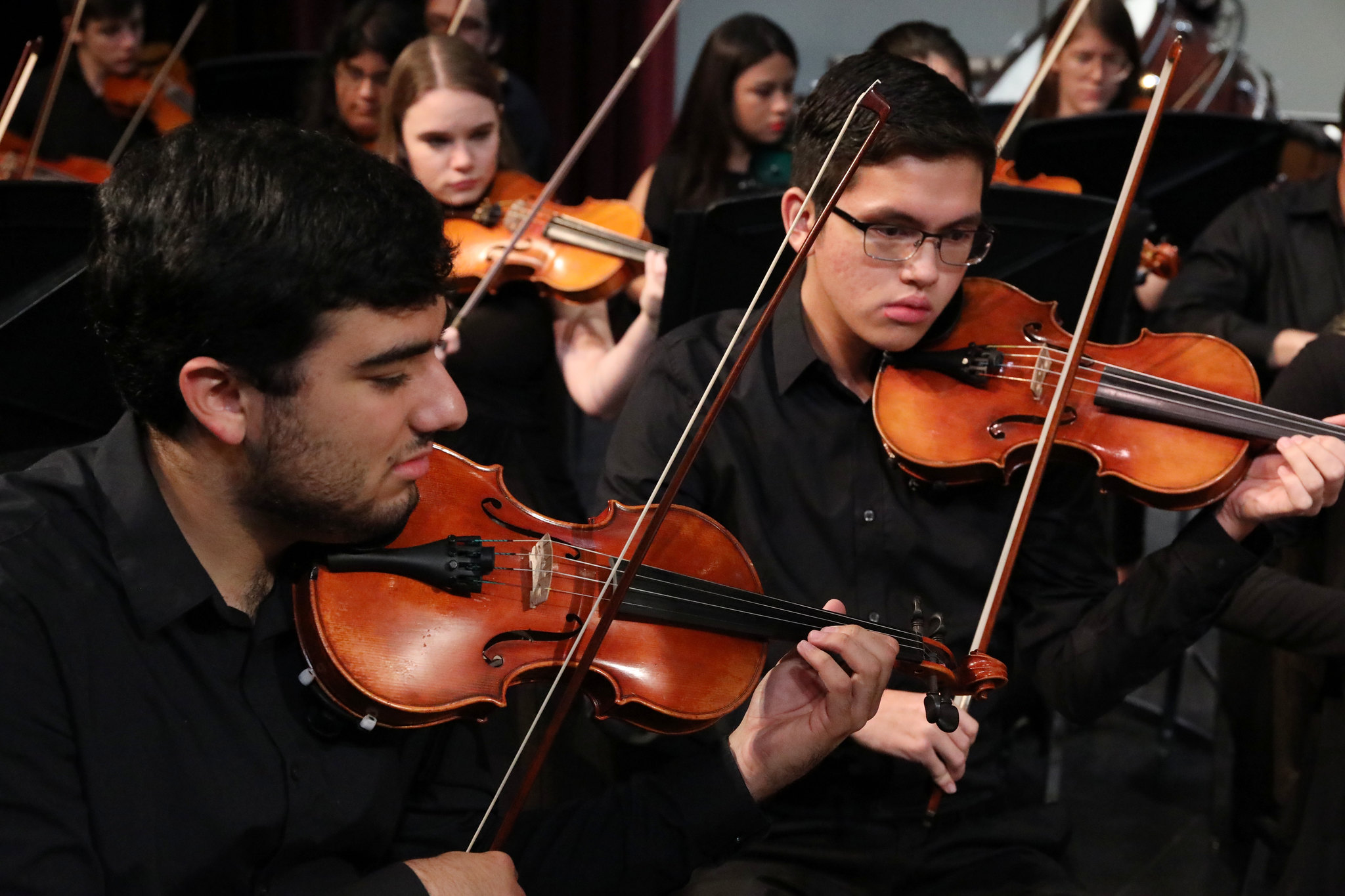 Two students dressed in all black while they play their violins at an orchestra performance