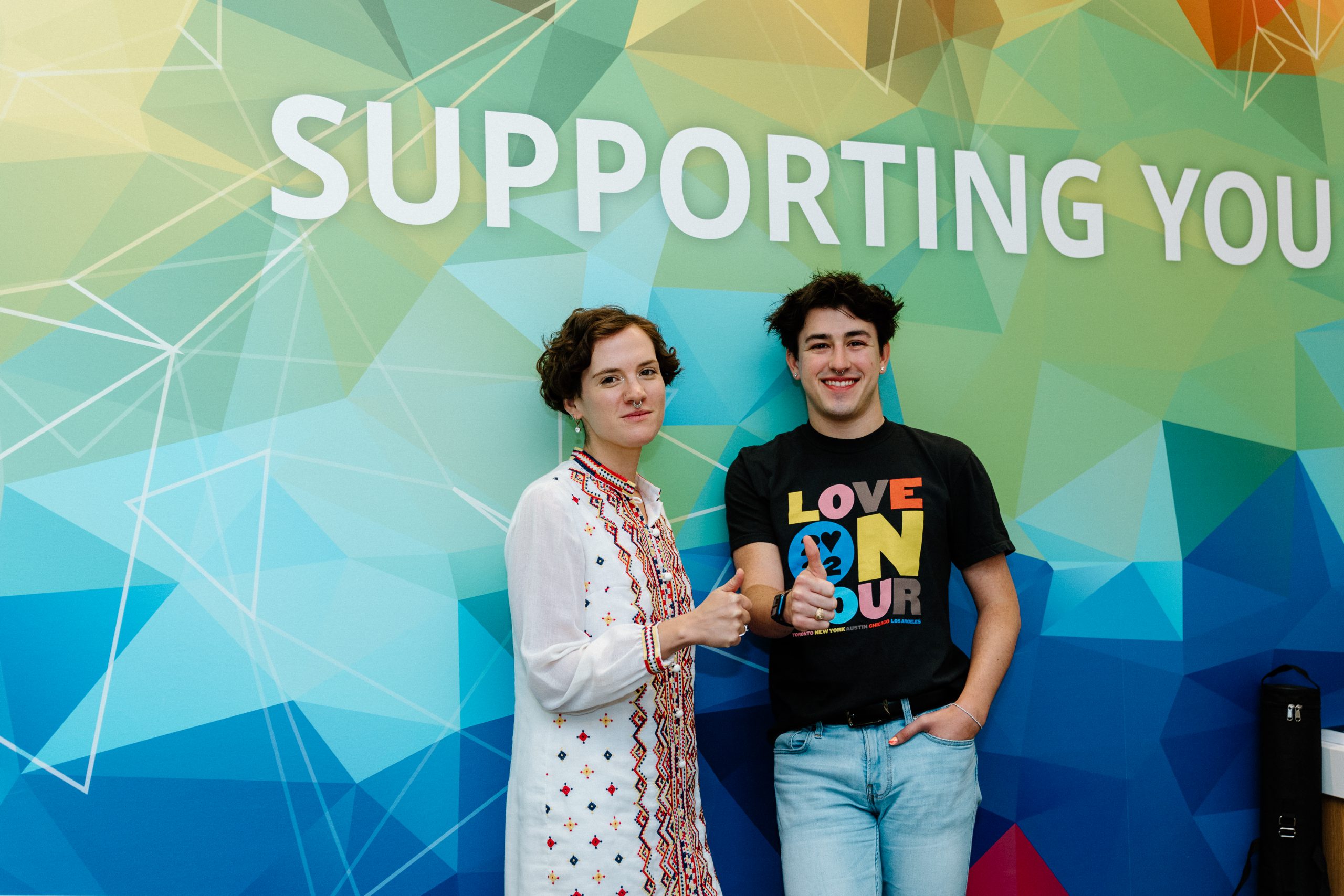 Image of Ben Gettleman ’23 and LGBTQ+ Pride Center Coordinator Frances Jackson in front of the Supporting You mural in the Student Services Building.