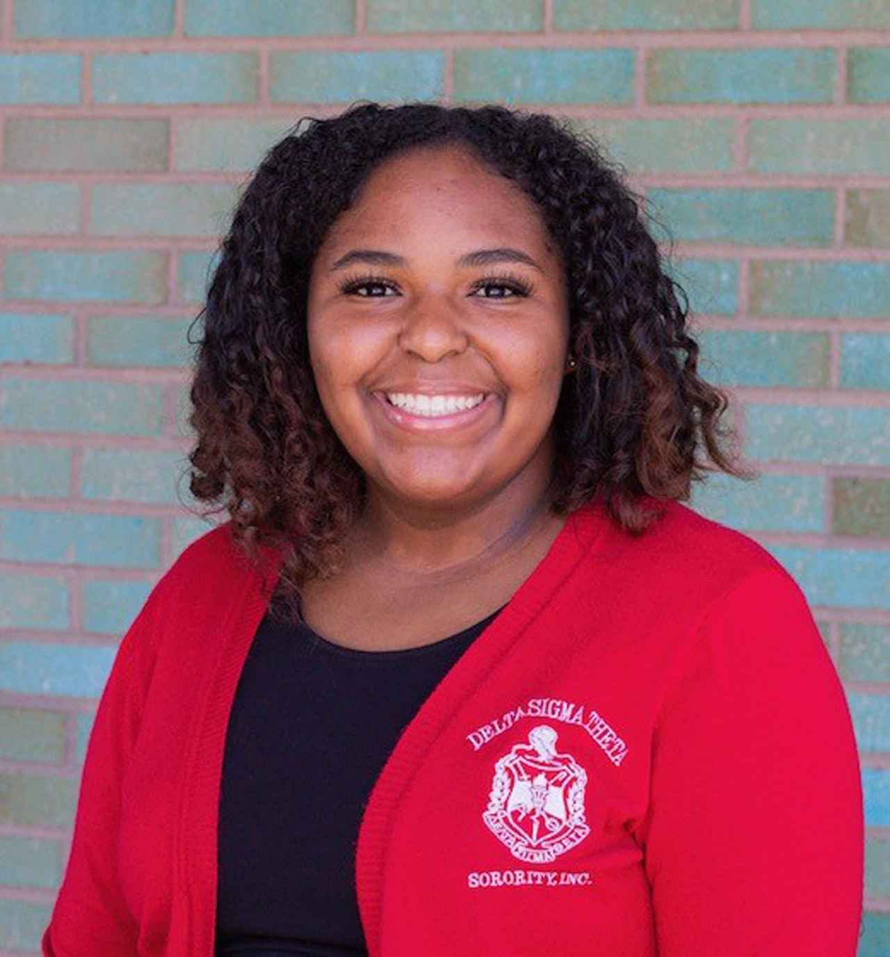 Jade McGhee stands in front of a brick wall in a red Delta Sigma Theta jacket