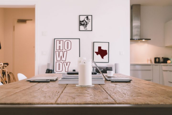 Apartment dining area with laptops and candles on a table. On the wall there are three frames: one that says howdy in block outlined letters, one of a collie, and one of the state of texas