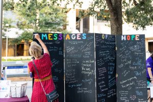 A woman in a red dress writes on the Messages of Hope board at the 2021 Suicide Awareness Month kickoff event