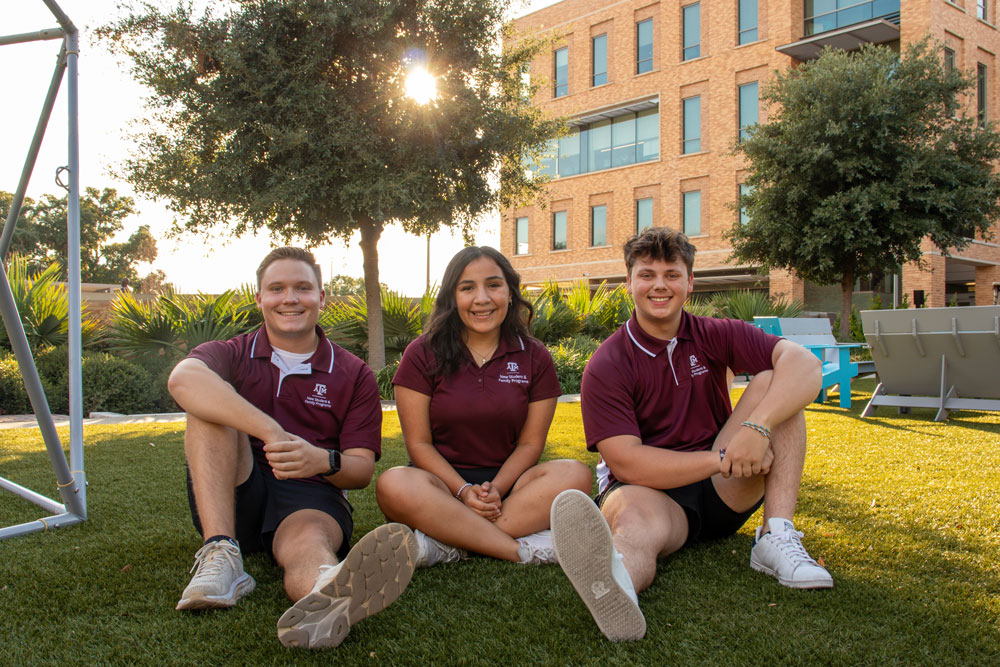 Three APFA members sitting on a lawn and smiling at the camera