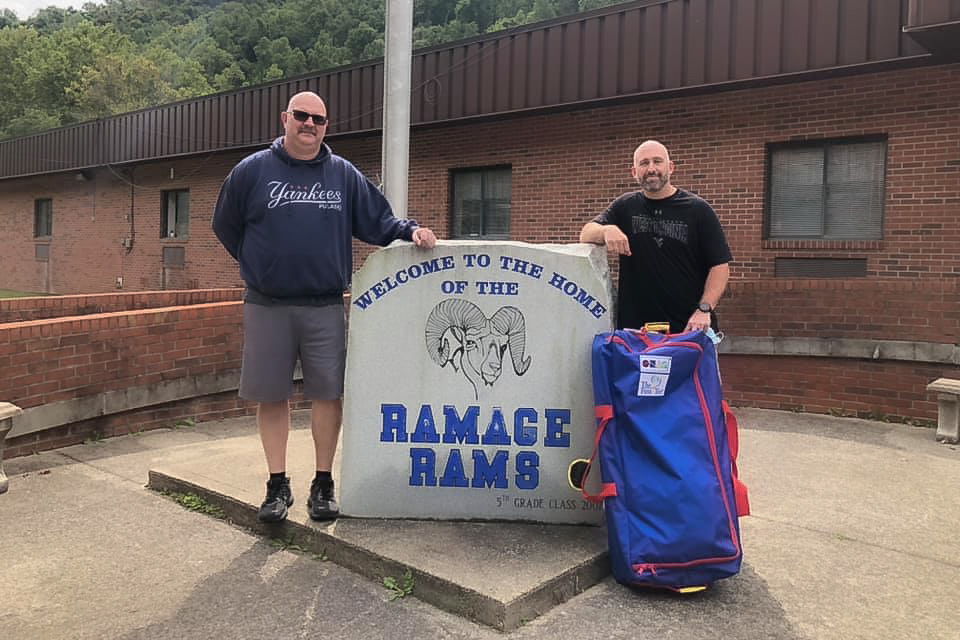 Brandon Burns and Daron Godby stand in front a Ramage Elementary next to a concrete sign the reads "Ramage Rams"