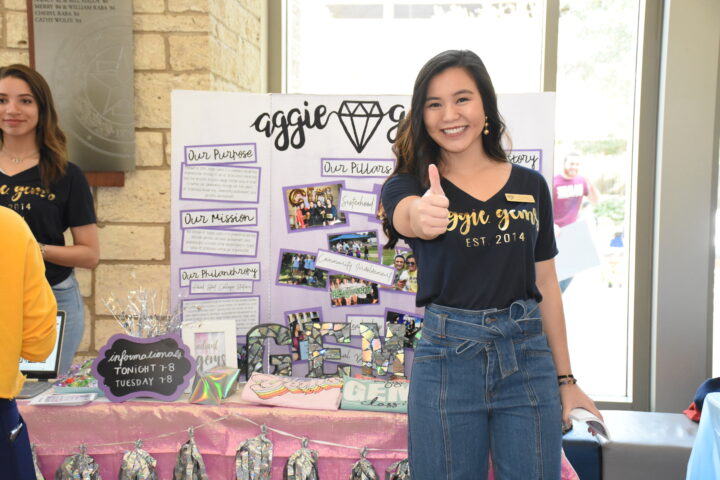 Aggie posing in front of a student organization table