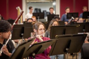 Kaitlyn Hawkins playing flute in a rehearsal room surrounded by other musicians