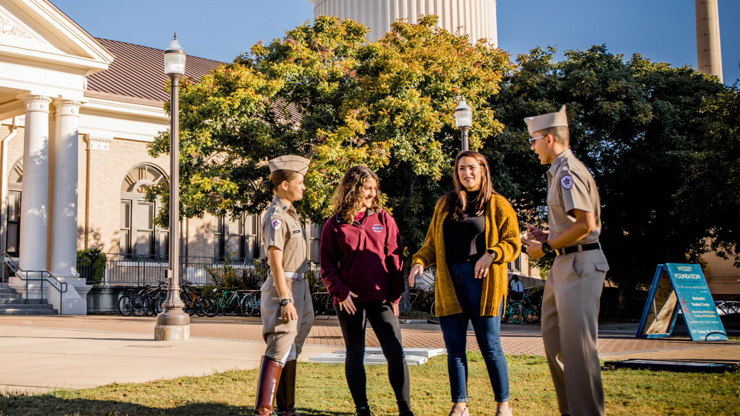 Four students, including two in Corps of Cadets uniforms, talking candidly in front of Sbisa.