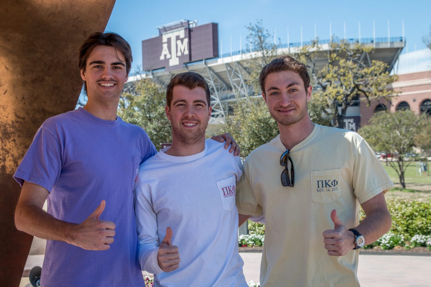 Three Pi Kappa Delta students posing under the Aggie Ring statue